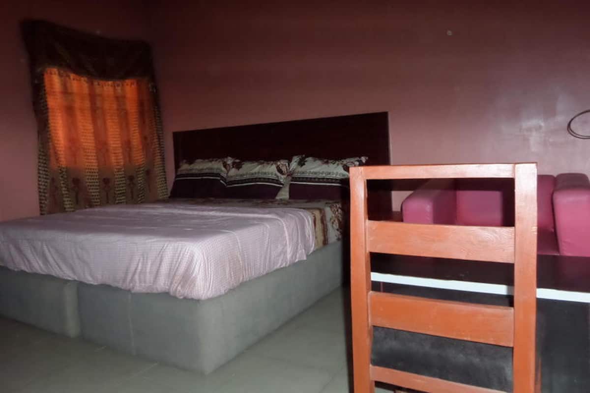 Un dormitorio con una cama, una silla de madera y un ventanal con cortinas.