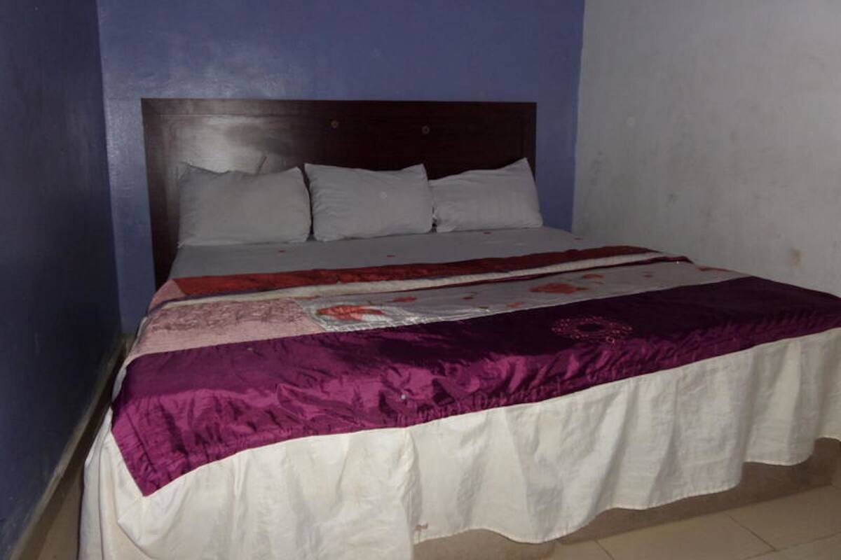 Una cama con cabecera de madera, ropa de cama blanca y una manta morada.