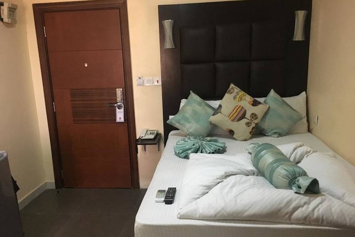 A hotel room with a bed, a bedside table, a telephone, and a door.