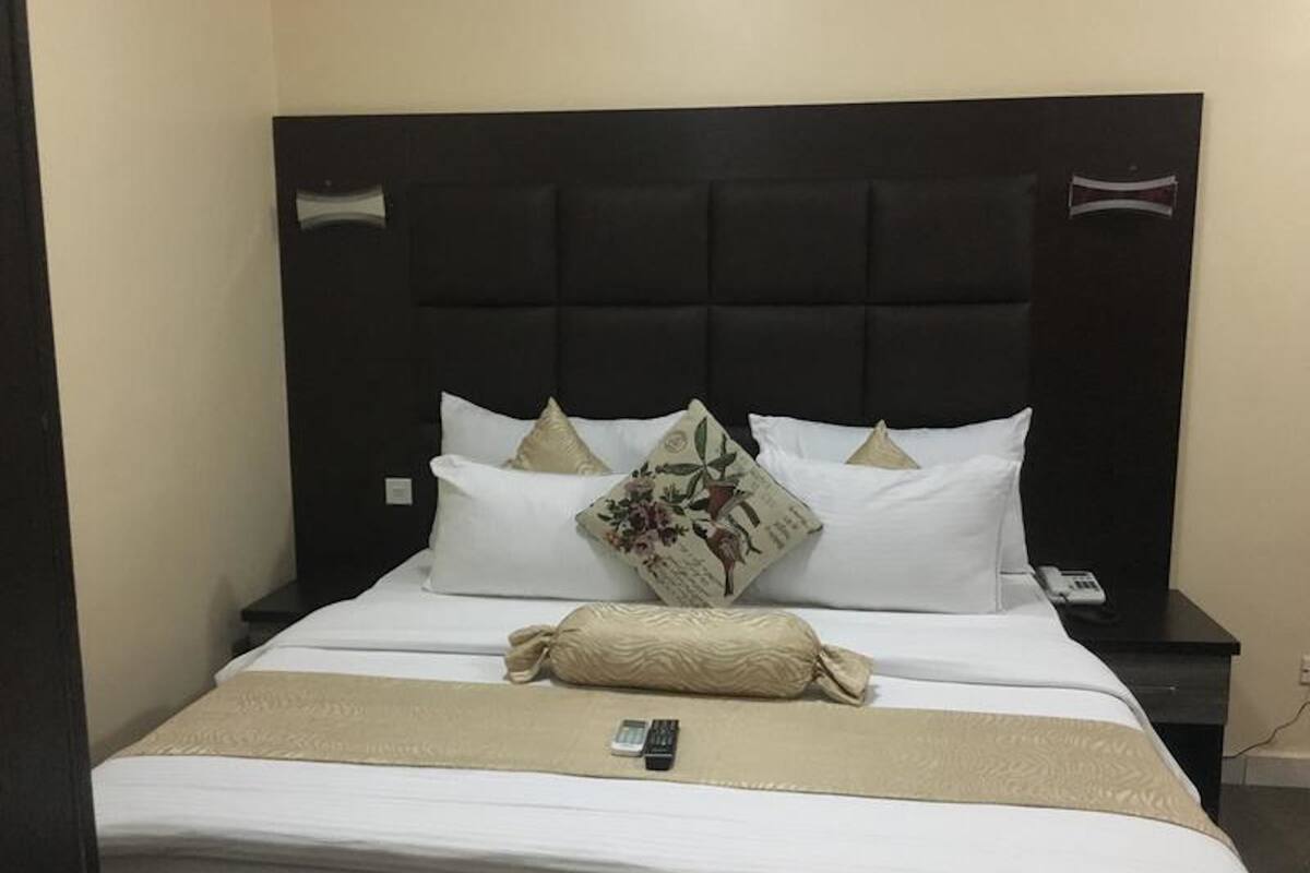 A neatly made bed with white linens, a beige throw blanket, and decorative pillows.