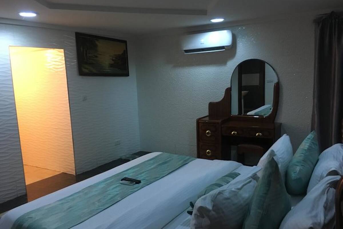 A hotel room with a bed, a dresser, a mirror, and a wall-mounted air conditioner.