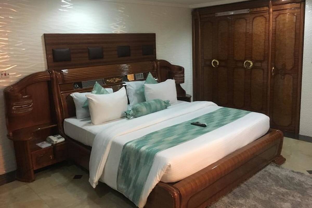 A bedroom with a wooden headboard, a large bed with multiple pillows, a nightstand, and a wardrobe.