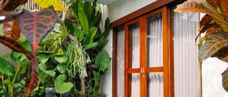 Una piscina con suelo de baldosas, rodeada de plantas tropicales y una puerta de madera con paneles de vidrio.