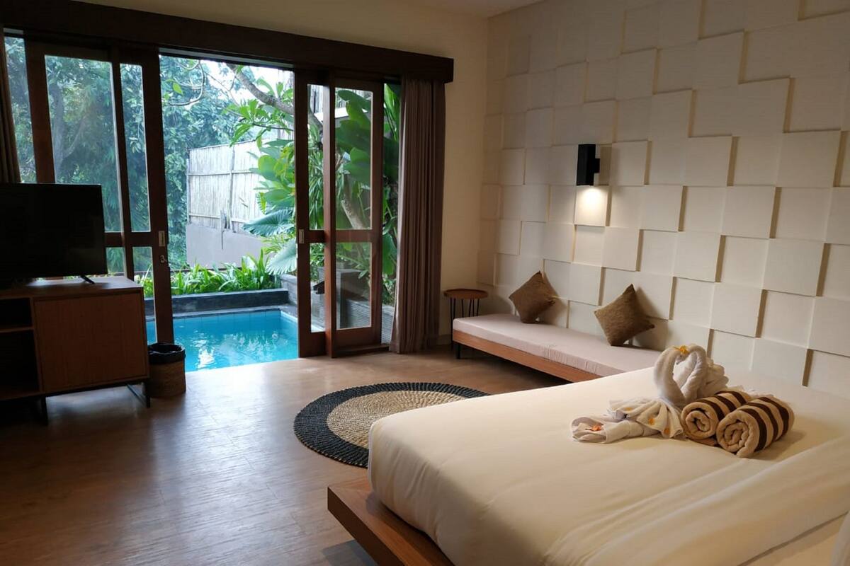 A hotel room with a bed, a TV, a pool view, and a wall with a unique pattern.