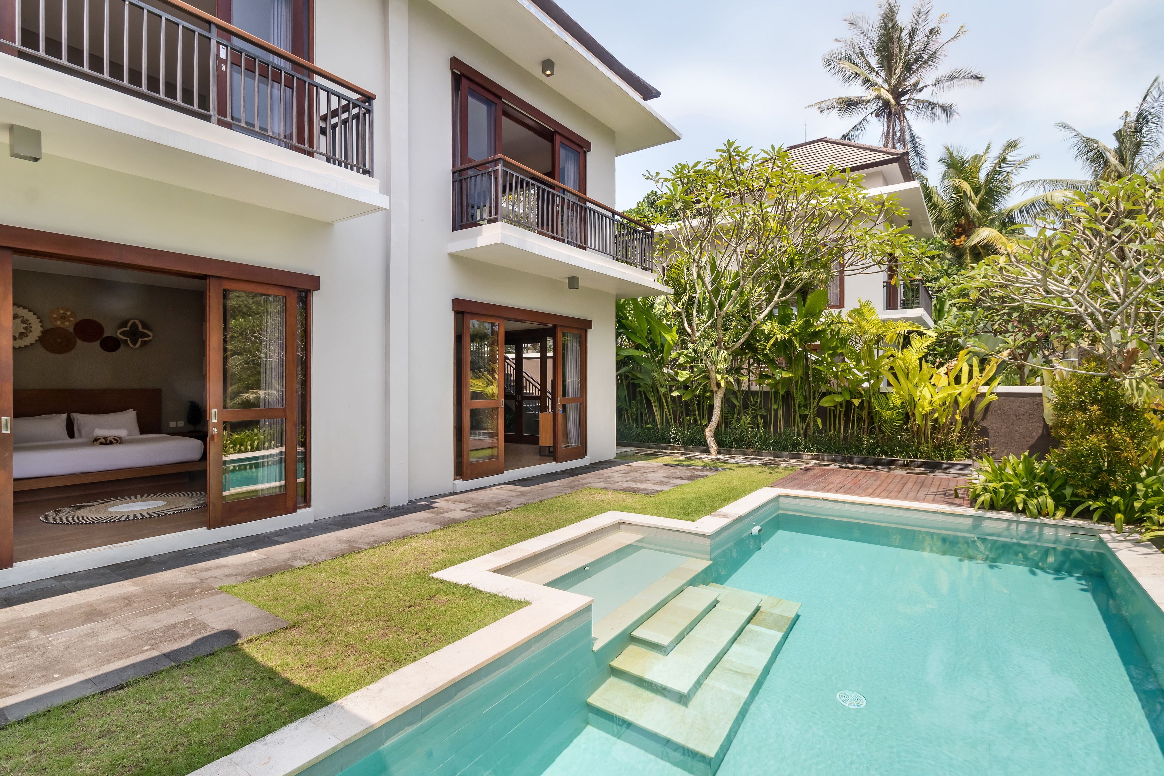A modern two-story house with a swimming pool, a balcony, and lush greenery.