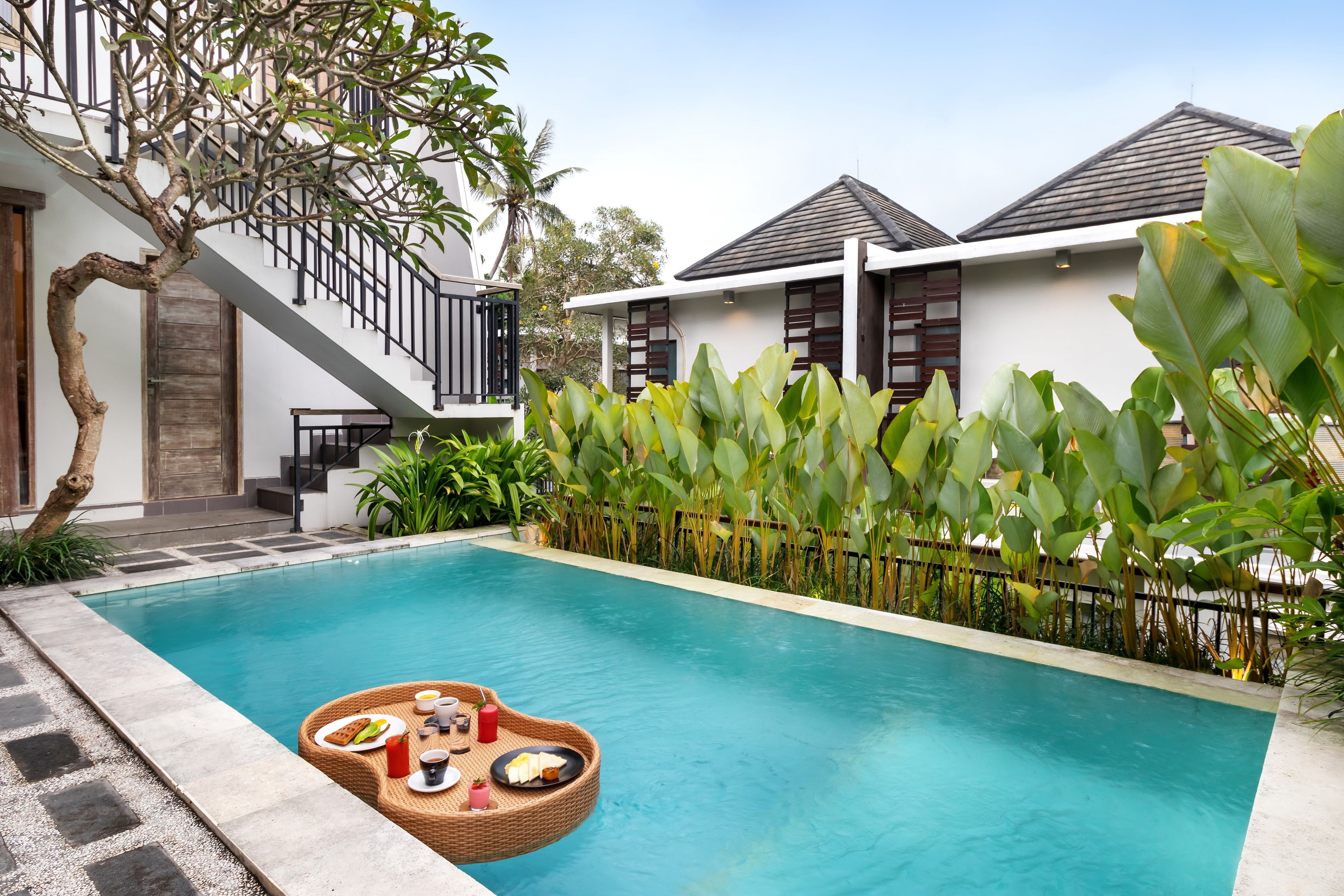 A swimming pool with a floating dining setup, surrounded by lush greenery and modern architecture.