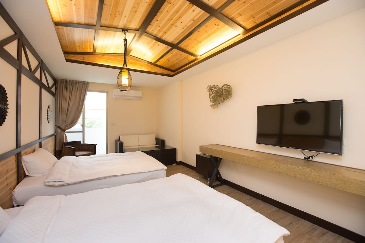 Habitación de hotel con dos camas, un televisor montado en la pared y techo de madera.