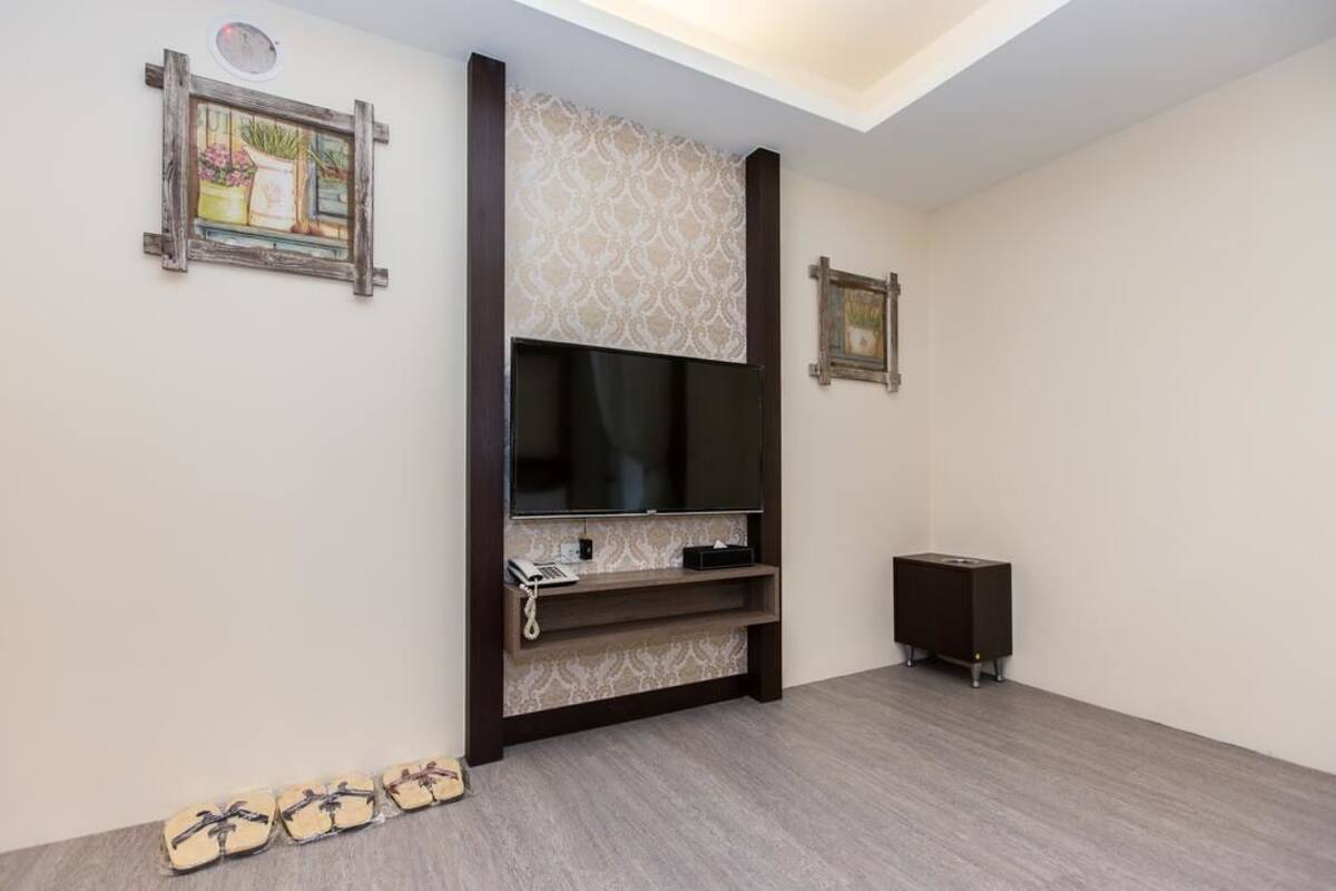 Una sala de estar con un televisor de pantalla plana montado en la pared, un mueble de madera debajo y un altavoz pequeño a la derecha.