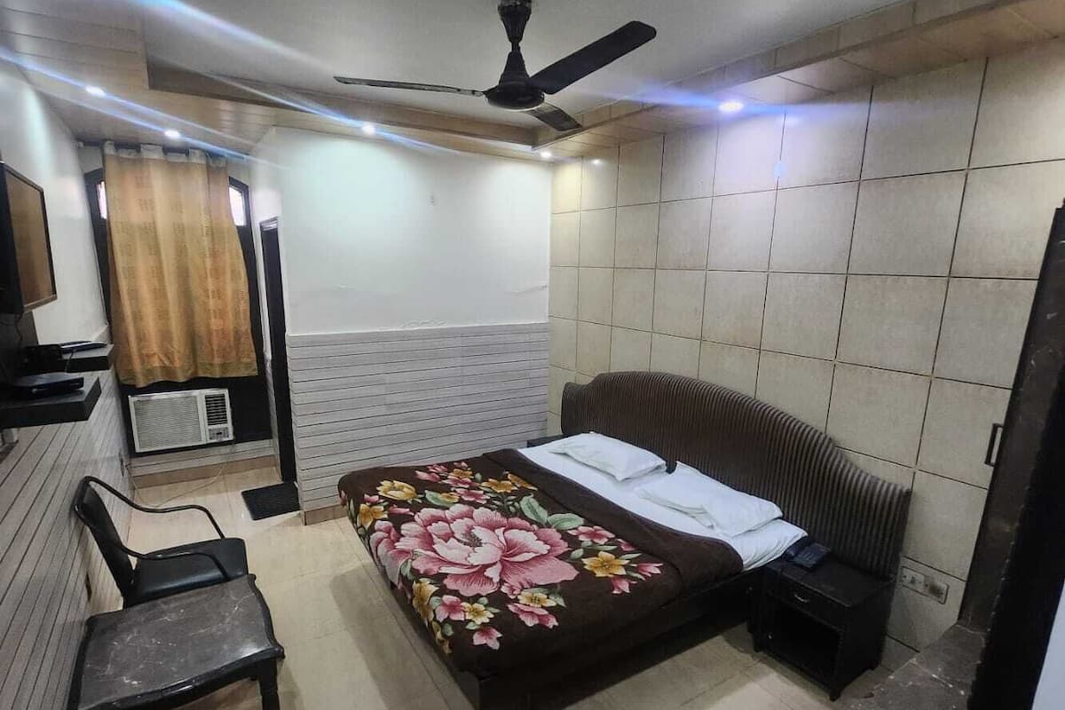 Ein Schlafzimmer mit einem Bett, einem Sessel, einem Schreibtisch, einem Deckenventilator und einem Fenster mit Vorhängen.
