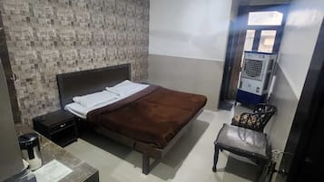 Un dormitorio con cama, una mesita, una silla, un calentador y una ventana.