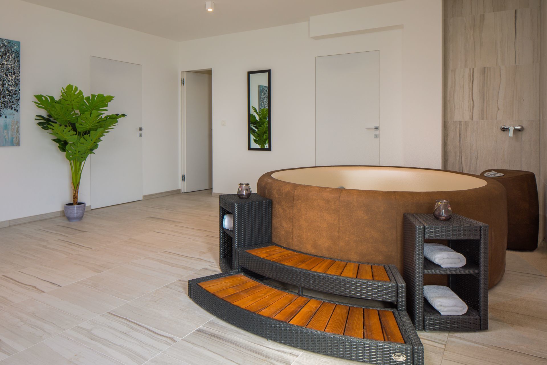 A modern spa room with a large, round hot tub, wooden steps leading to it, and a potted plant.