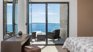 A bedroom with a large bed, a desk with a chair, a small ottoman, and a view of the sea through a sliding glass door. - Trogir Pearl Luxury Resort (Okrug)
