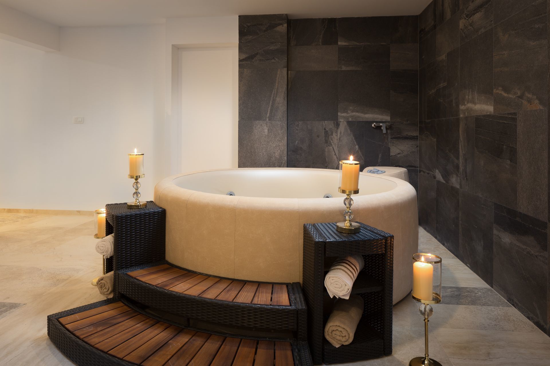 Un baño moderno con una bañera independiente, paredes de piedra oscura y un banco de madera.