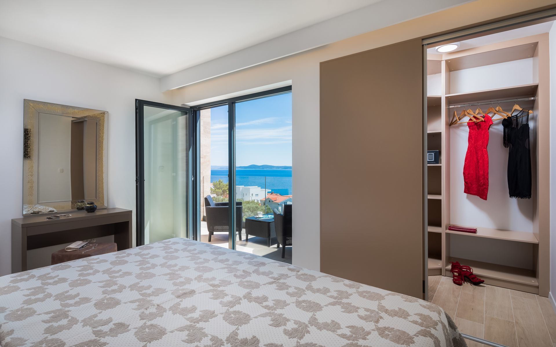 Ein Hotelzimmer mit Bett, Schreibtisch, Spiegel, Kleiderschrank und einem Balkon mit Meerblick.