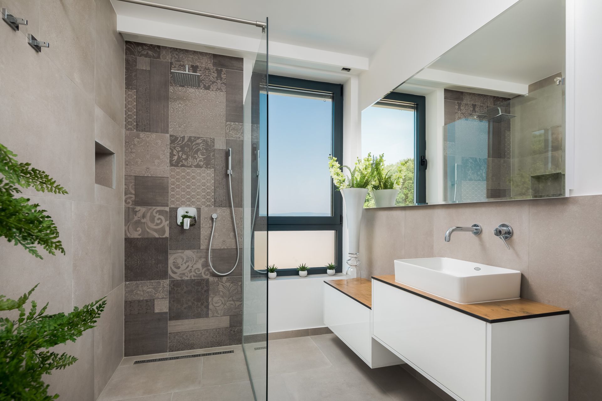A modern bathroom with a glass-enclosed shower, a white sink, and a window with a view.