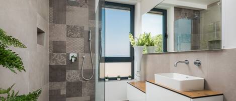 A modern bathroom with a glass-enclosed shower, a white sink, and a window with a view.