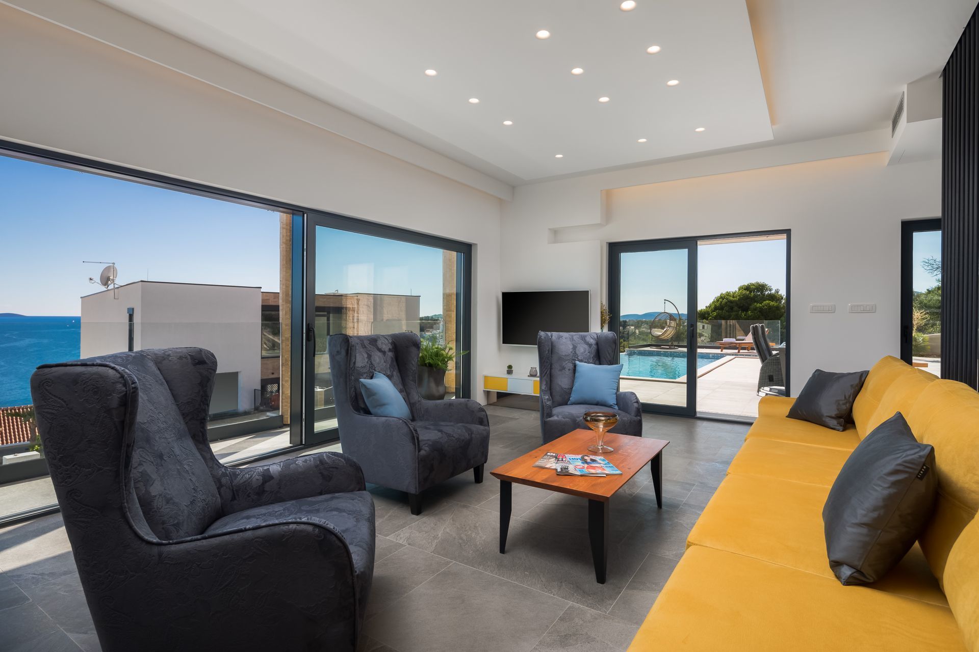 A modern living room with a large window, a sofa, two armchairs, a coffee table, and a TV.
