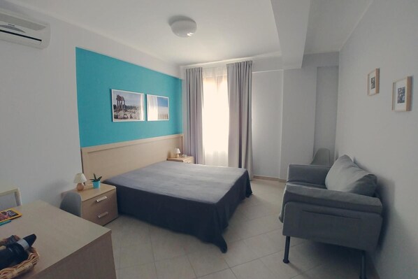 Un dormitorio con cama, escritorio, silla y ventana con cortinas.