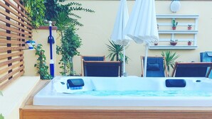 A hot tub with wooden steps, surrounded by potted plants and outdoor furniture.