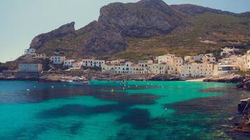 Une ville côtière avec des bâtiments qui bordent le front de mer, une eau turquoise et limpide, et une montagne rocheuse en arrière-plan.