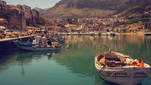 A harbor with boats docked, a mountainous backdrop, and buildings along the waterfront.