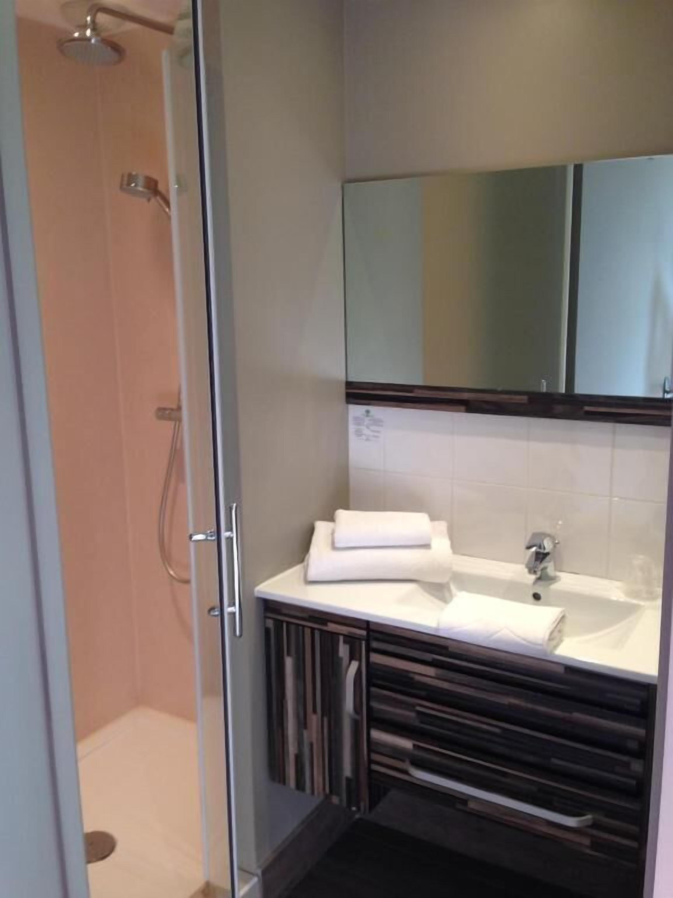 Une salle de bain avec une douche à parois de verre, un lavabo blanc avec une serviette, et un miroir au-dessus du lavabo.