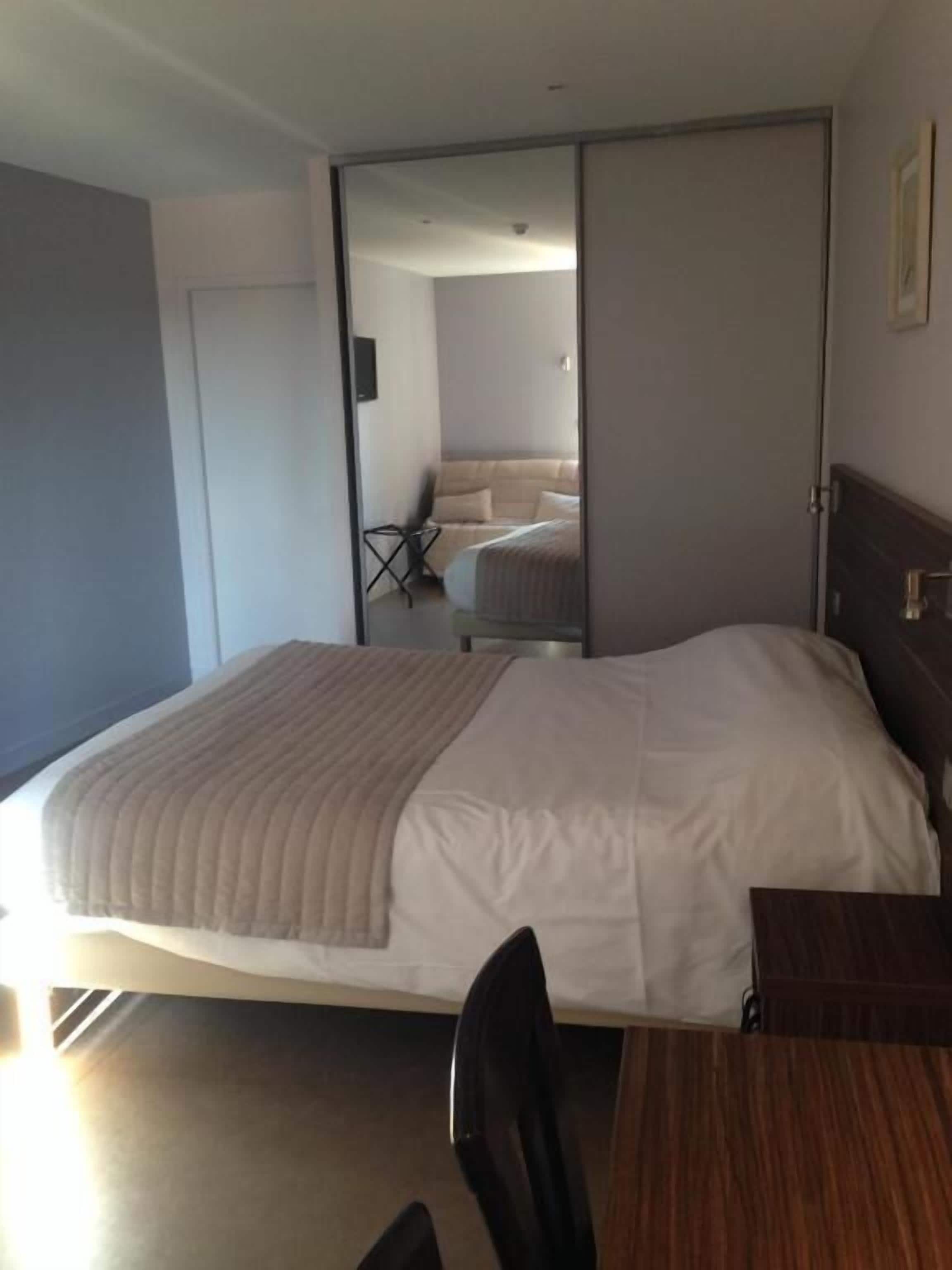Ein Hotelzimmer mit einem Bett, einem Schreibtisch und einem Stuhl. Eine Schiebetür führt zu einem anderen Raum.
