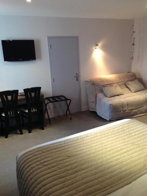 Un dormitorio con cama, escritorio, silla, televisor y puerta.