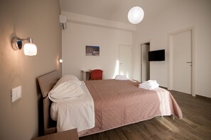 A modern bedroom with a large bed, a bedside table, a red chair, a flat-screen TV mounted on the wall, and a ceiling light fixture. - La Terrazza di Harmakhis (Partanna)