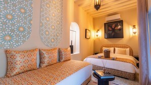 A hotel room with a patterned sofa, a bed with a patterned headboard, and decorative wall art. - Riad Dar Tiflet (Marrakech)