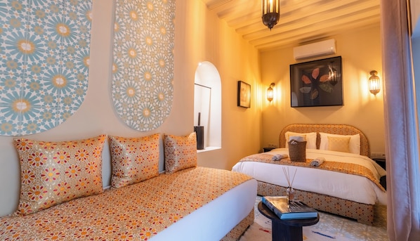 A hotel room with a patterned sofa, a bed with a patterned headboard, and decorative wall art.