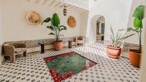 A room with patterned floor tiles, a central green area with red flowers, potted plants, and a decorative wall. - Riad Dar Tiflet (Marrakech)
