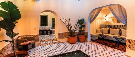 A cozy interior with a patterned floor, a seating area with cushions, and potted plants.