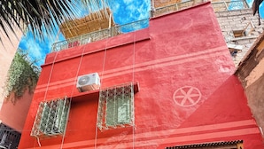 A red building with a wooden door and windows, potted plants in front, and a blue sky in the background. - Riad Dar Tiflet (Marrakech)