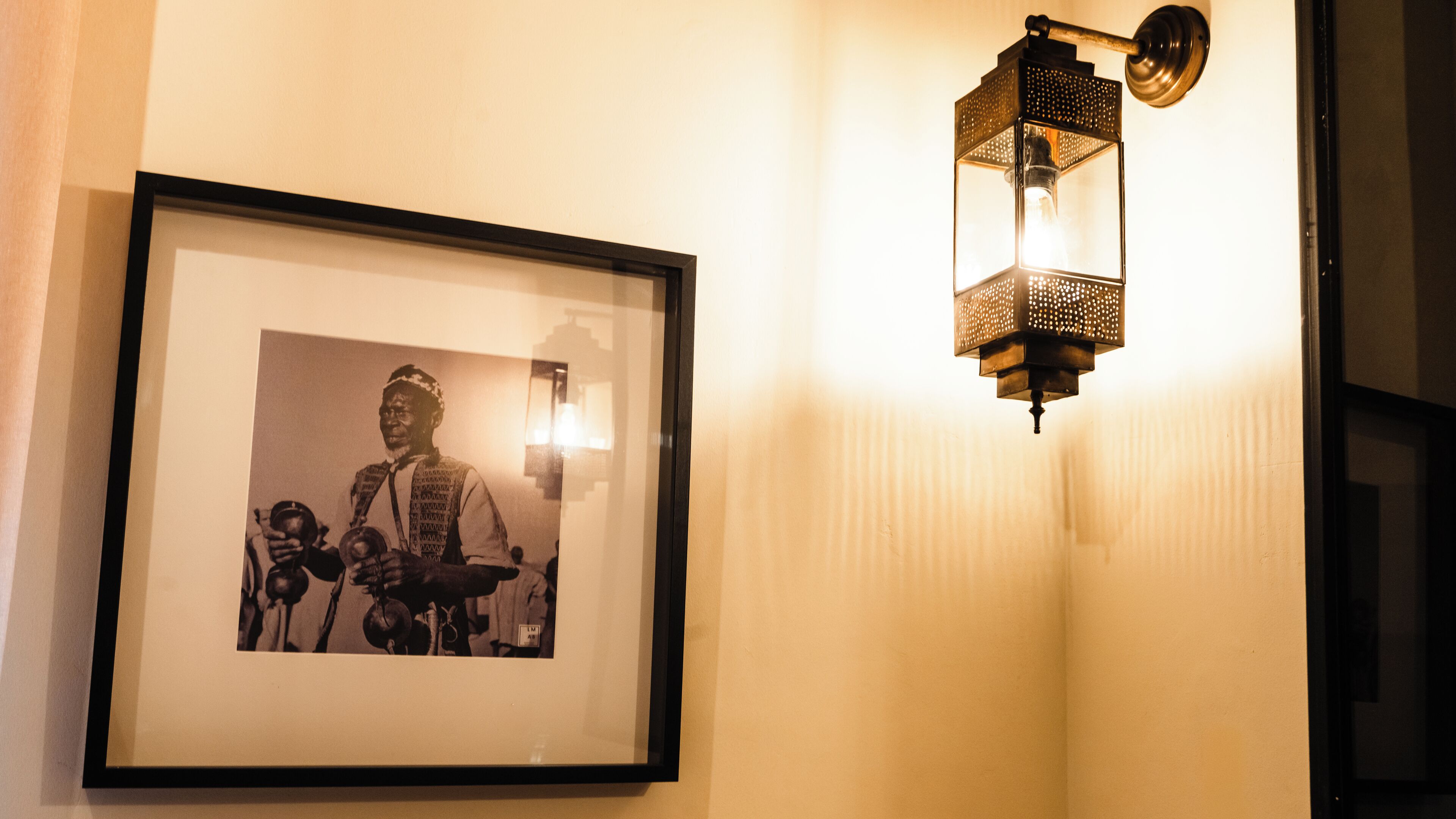 A framed black and white photograph on a wall, a wall-mounted light fixture, and a door frame.