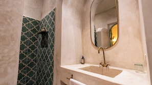 A bathroom with a beige sink, a gold faucet, and a green patterned shower wall.