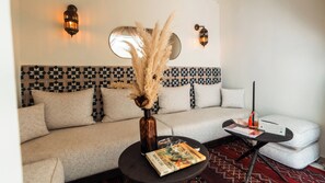 Un salon moderne avec un mur orné d’un motif, un canapé, une table basse avec un livre, et des appliques murales décoratives.
