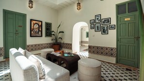 A hotel lobby with a sofa, ottoman, potted plant, and framed pictures on the wall. - Riad Dar Tiflet (Marrakech)