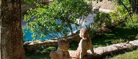Une sculpture représentant deux personnages, placée au bord d’une piscine, entourée de verdure et d’un mur de pierre.