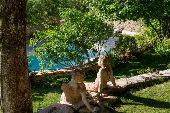 A sculpture of two figures by a poolside, surrounded by greenery and a stone wall.