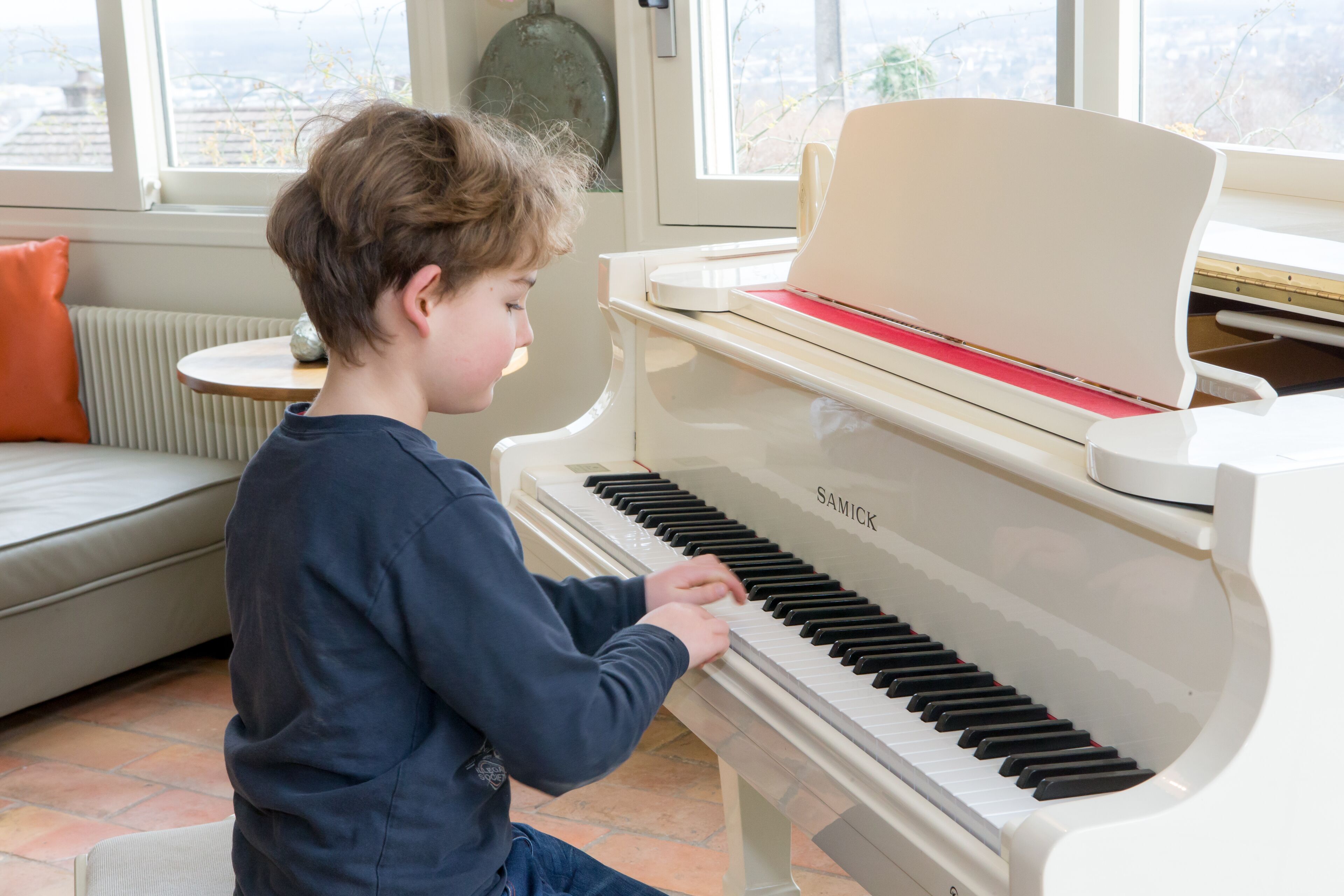 A child playing a white piano with the brand name "SAMICK" visible.