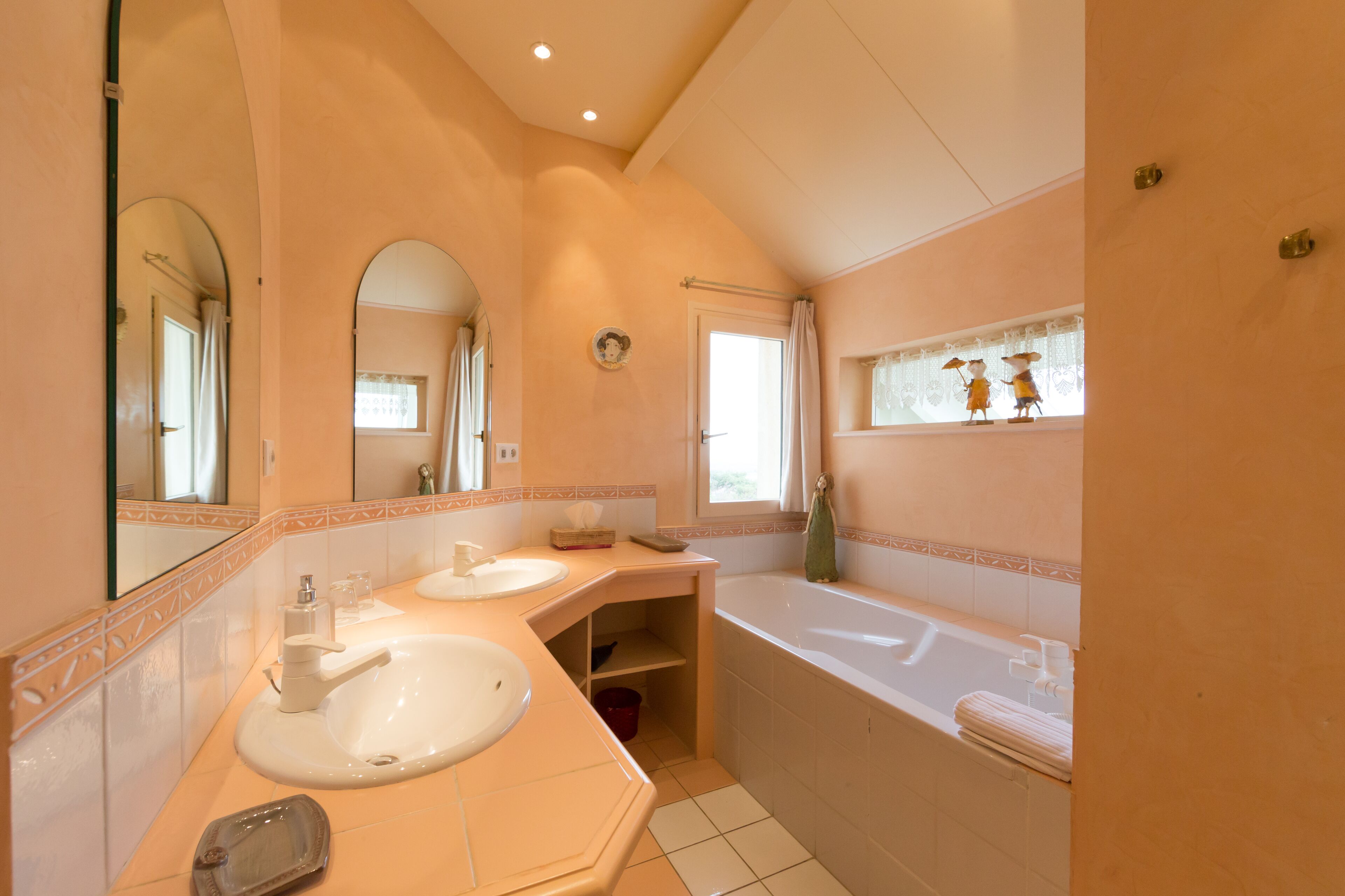 A bathroom with two sinks, a bathtub, and a window with decorative figures.