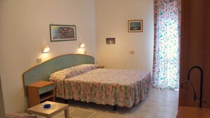 A small, cozy room with a bed, a desk, and a chair. There are two wall-mounted lamps and a window with floral curtains. - Hotel Vecchia Rimini (Comacchio)