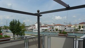 A balcony with a view of a river and buildings. There is a table and chairs on the balcony. - Hotel Vecchia Rimini (Comacchio)