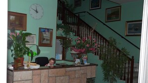 A reception desk with a clock, framed pictures, and potted plants. - Hotel Vecchia Rimini (Comacchio)