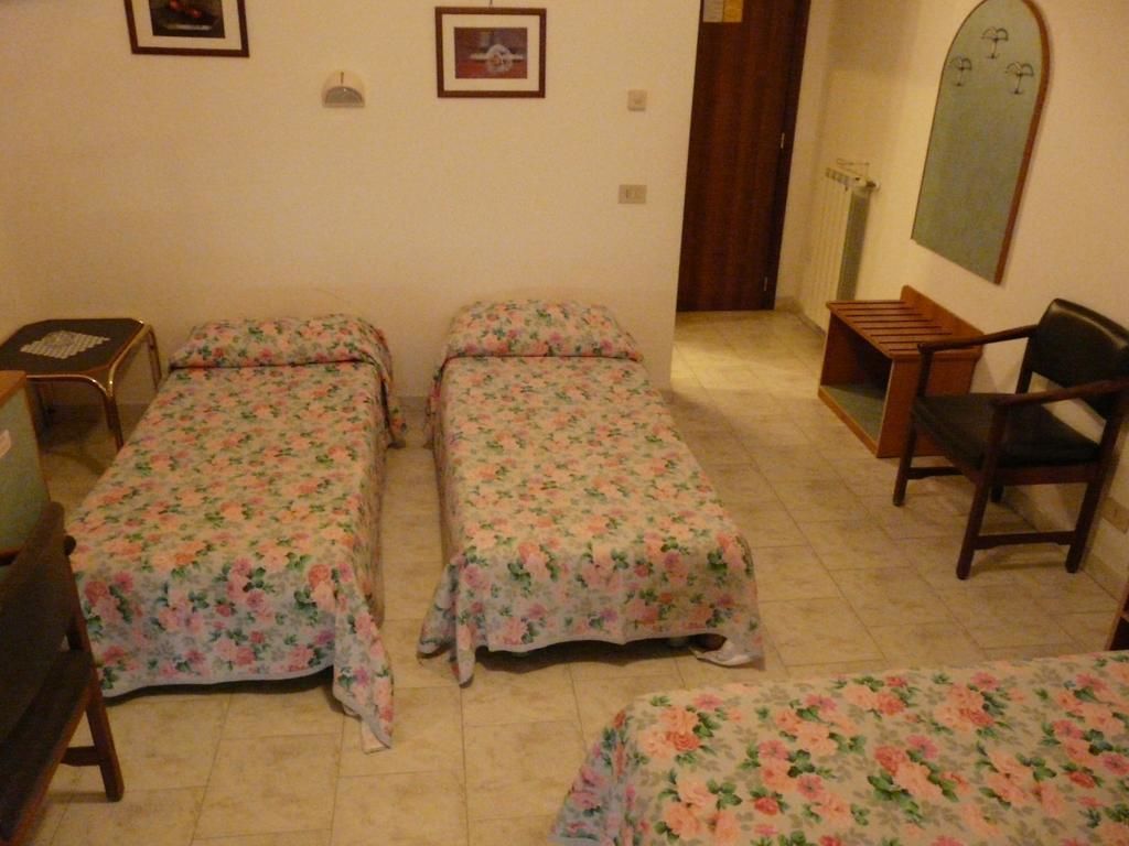 A room with two single beds with floral bedding, a wooden chair, a small table, and a mirror on the wall.
