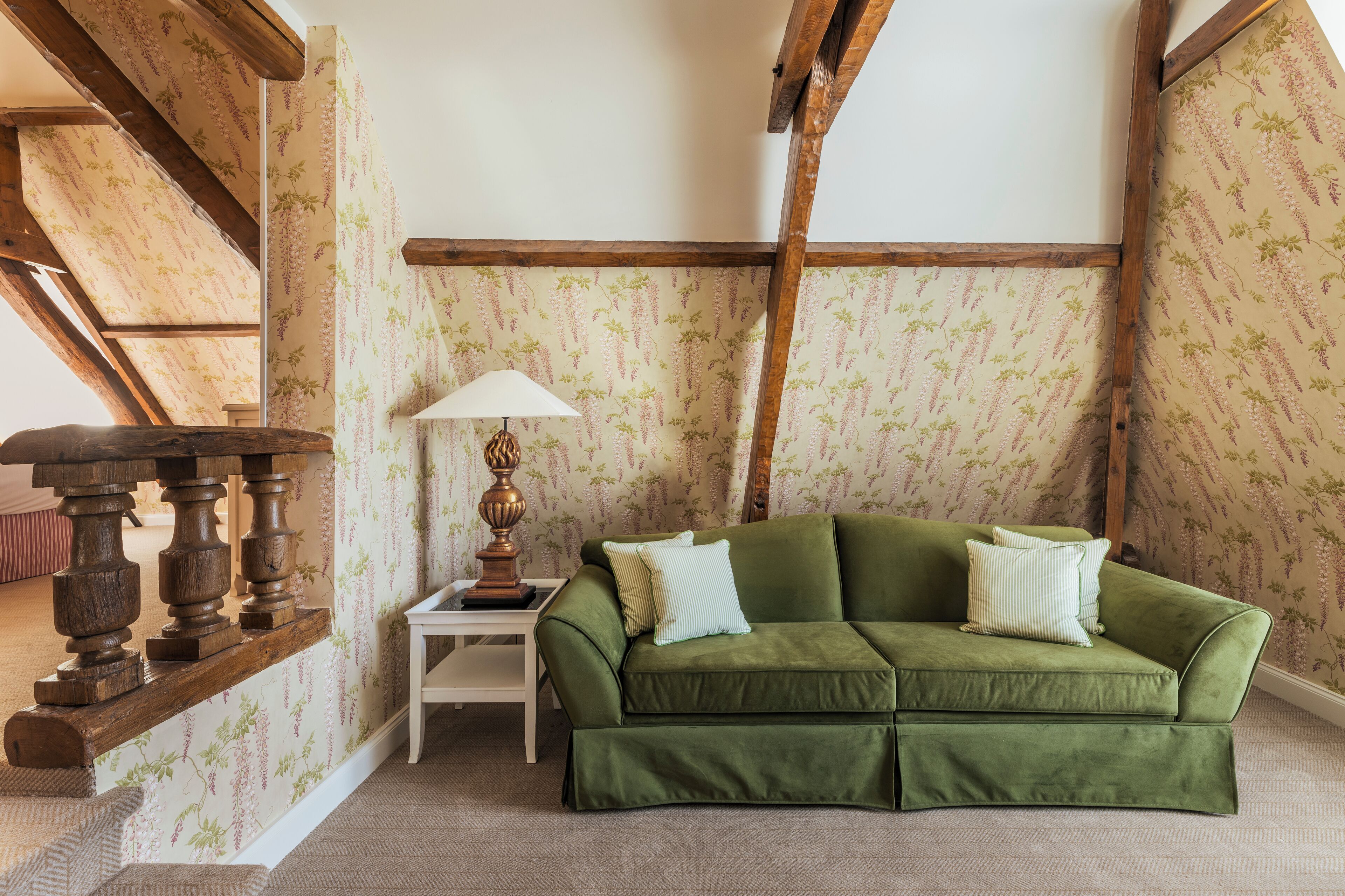 A green sofa with two pillows, a small table with a lamp, and a staircase with wooden beams.