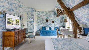 A bedroom with a TV, wooden dresser, blue bed, and a wooden ceiling beam.