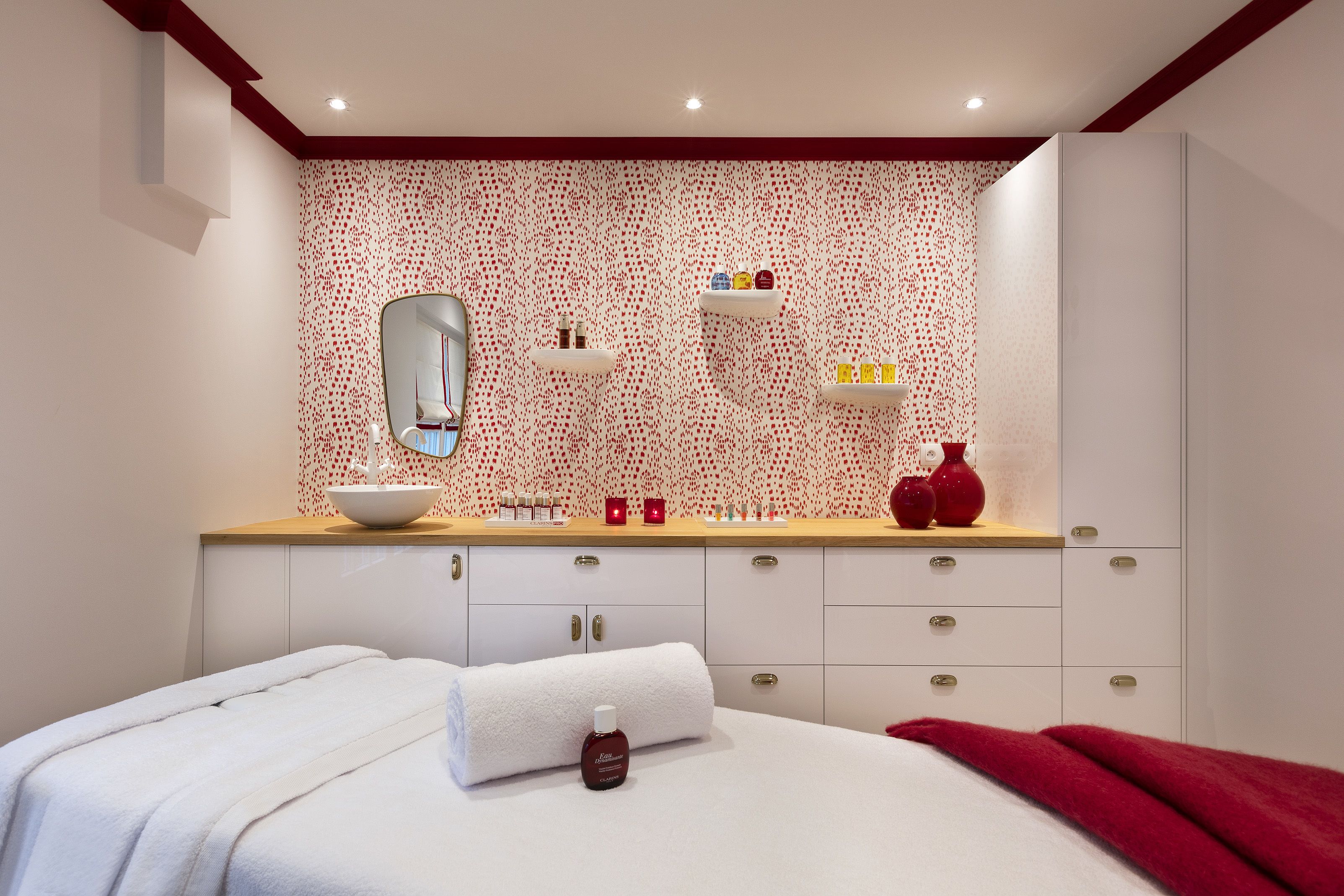 A modern bathroom with a large mirror, white cabinets, and a red patterned wall.