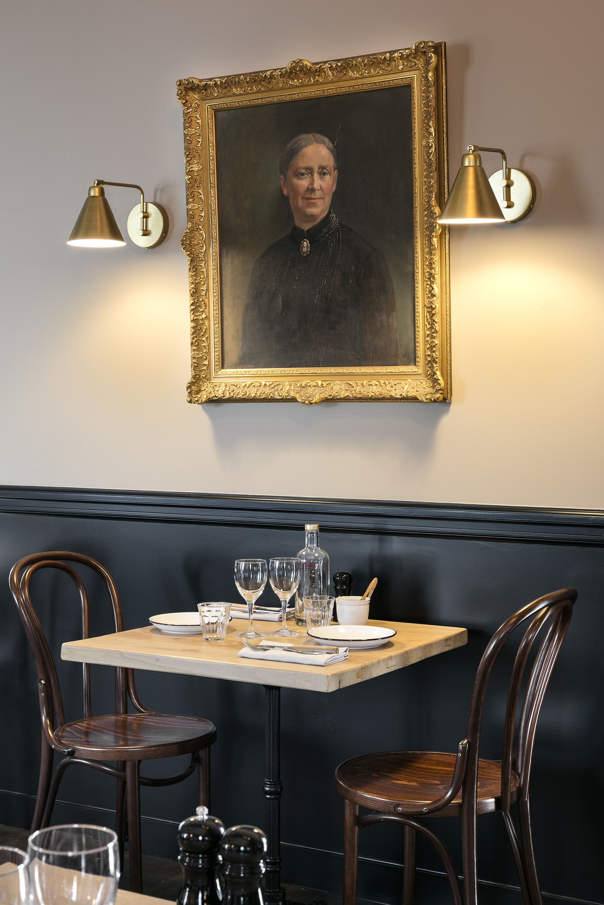 En matplats med ett bord dukat för två personer, två stolar, ett inramat porträtt på väggen och två vägglampor.